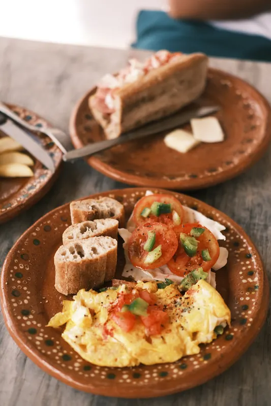 Œufs brouillés, tartines à la tomate et café dans de la vaisselle en terre cuite.