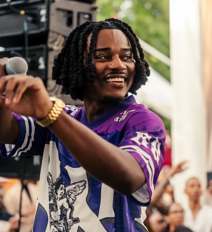 Un chanteur souriant, micro à la main, chemise violette et blanche, devant le public.
