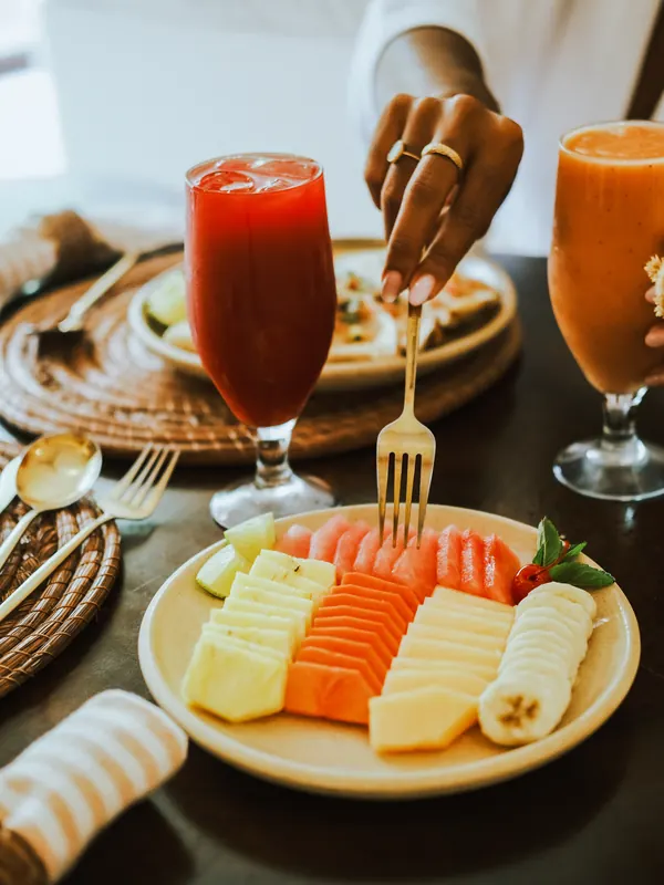 Une main pique un morceau de fruit, entre deux verres de jus frais.