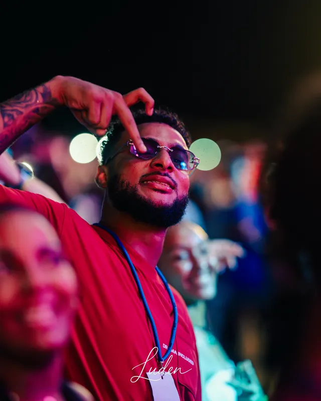 Un homme à lunettes rouges lève le bras dans la foule, les lumières de la fête en arrière-plan.