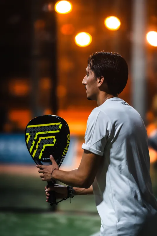 Un joueur de padel, de profil, raquette en main, sur un terrain éclairé le soir.