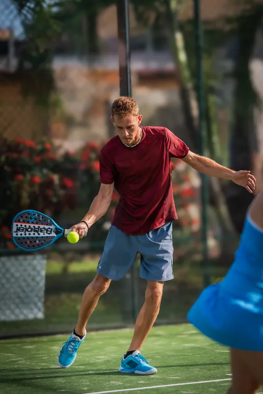 Un joueur de padel en t-shirt rouge se prépare à frapper, sur un terrain en extérieur.