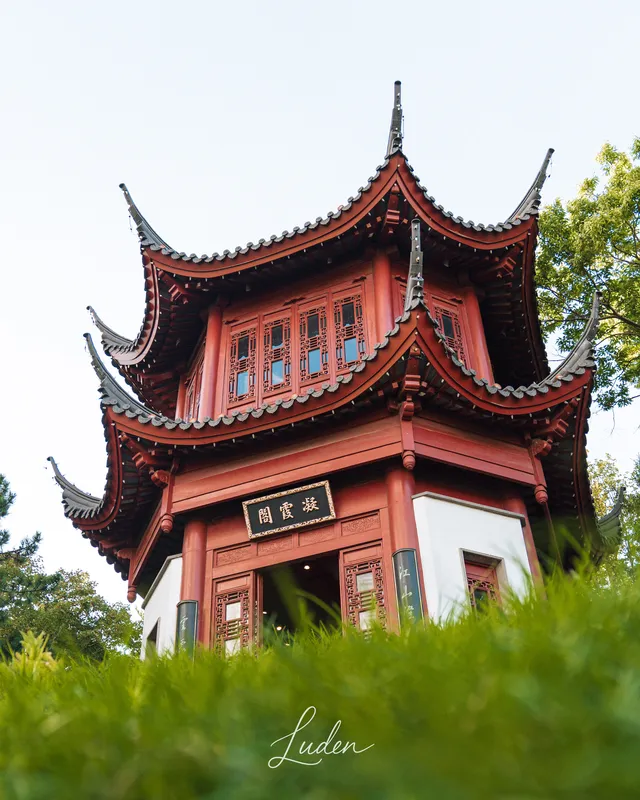 Une pagode rouge aux toits relevés, vue d’en bas au-dessus de l’herbe.