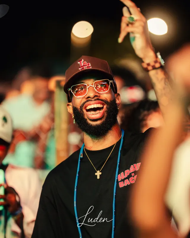 Un homme à casquette et lunettes rouges éclate de rire au milieu du public, un badge autour du cou.