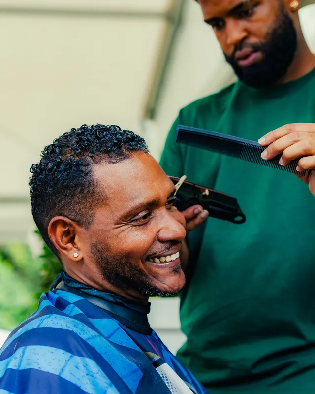 Un client souriant pendant sa coupe, le coiffeur en vert tient un peigne.